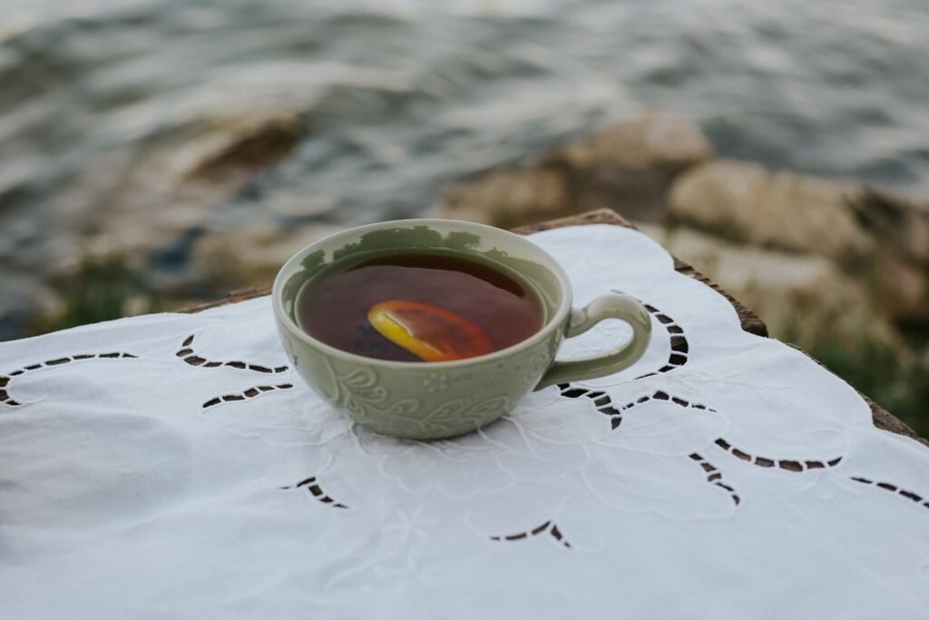 A cup of tea with a lemon slice on white lace cloth beside the water