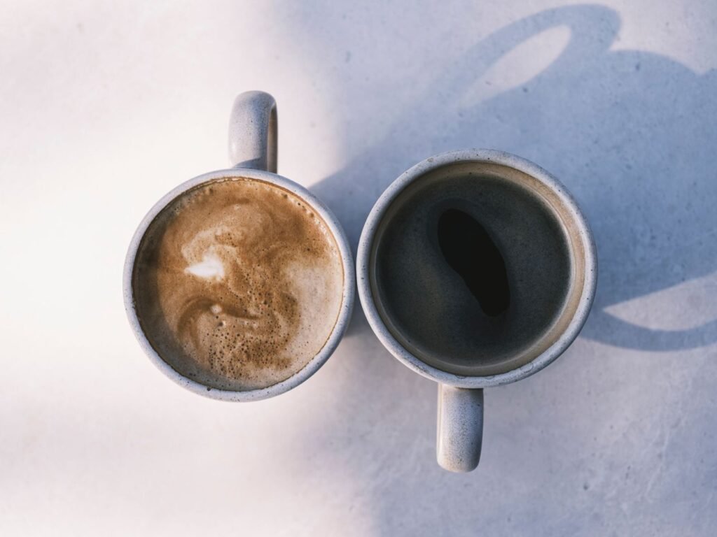 A milky coffee and a black coffee casting shadows on a pale table