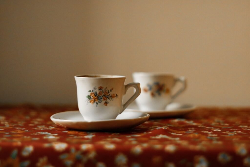 Two floral teacups on a red patterned tablecloth