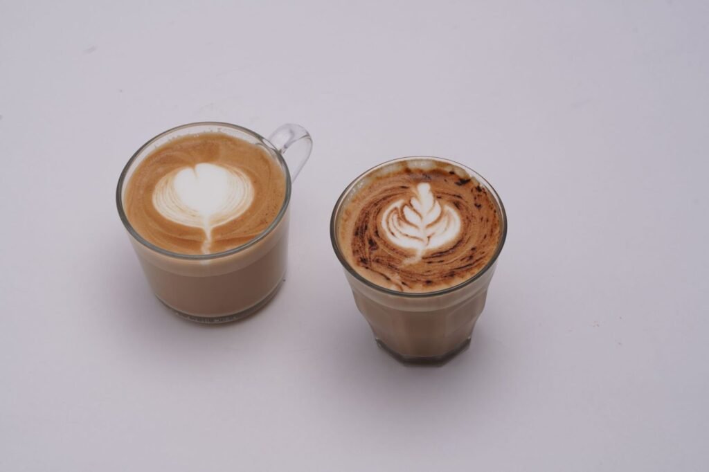 Two glasses of coffee with heart and leaf patterns in the foam
