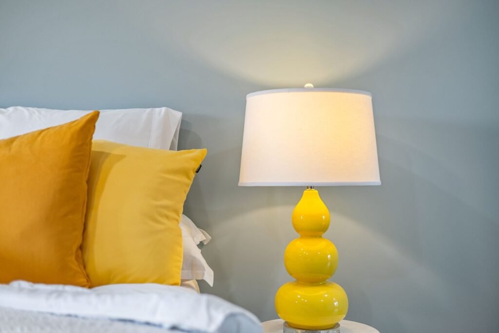 Yellow bedside lamp and cushion beside white bedding