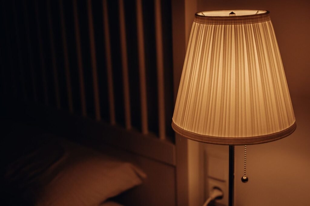 Warm light shining through a pleated lampshade beside a bed