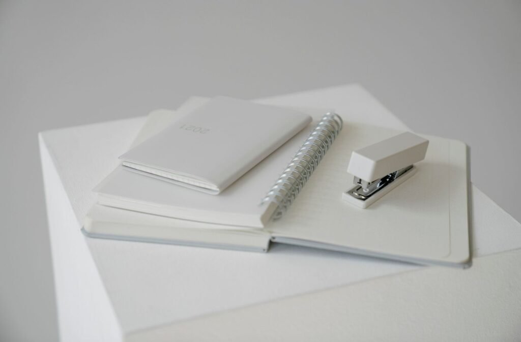 White notebooks and a stapler arranged on a pale surface