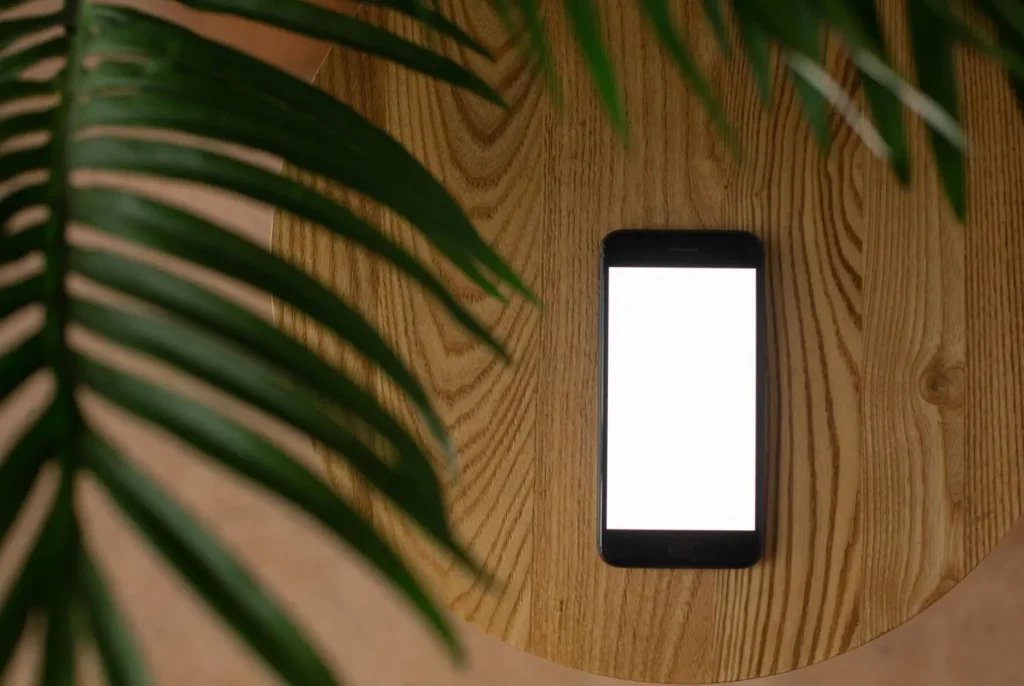 Smartphone with a blank white screen on wood beside green palm leaves