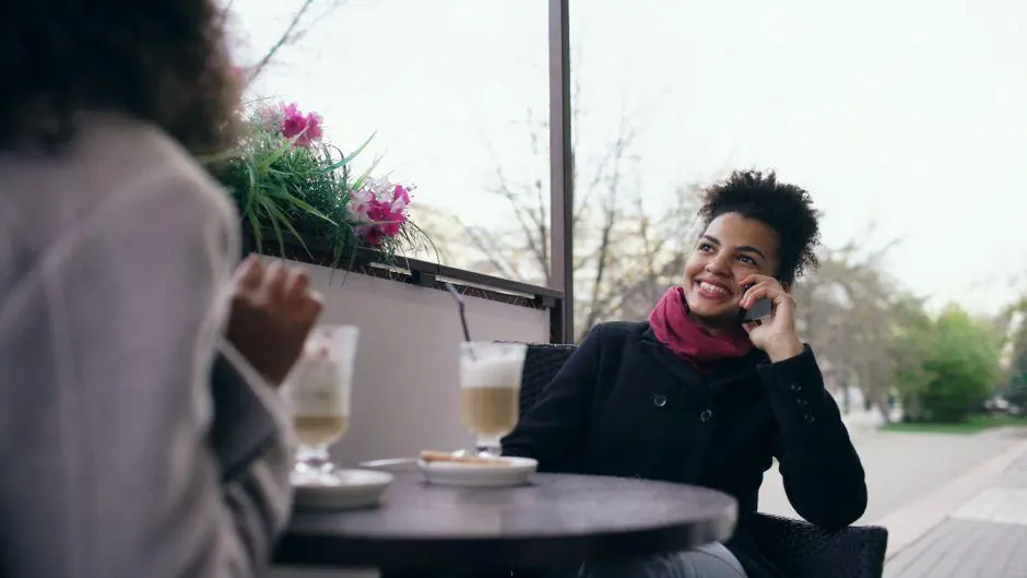 Woman using a phone at a cafe table with another person