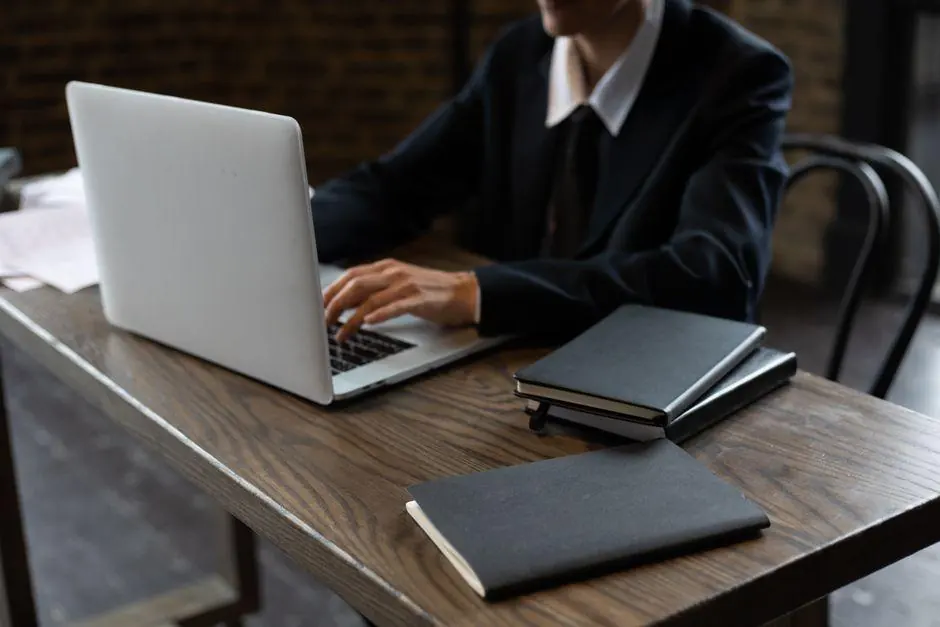 Person using a laptop with closed notebooks on the table
