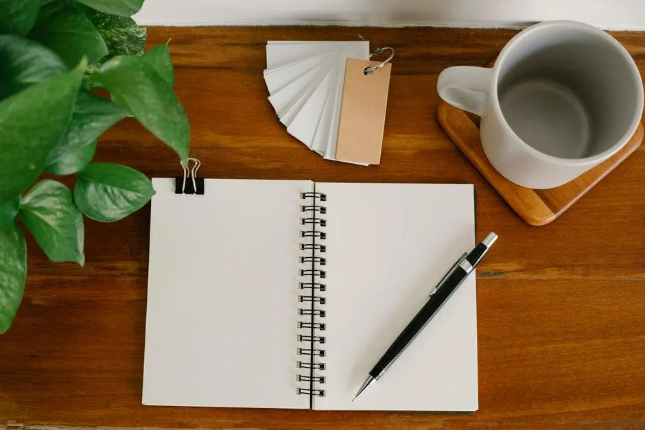 Blank notebook and pen beside a mug and plant