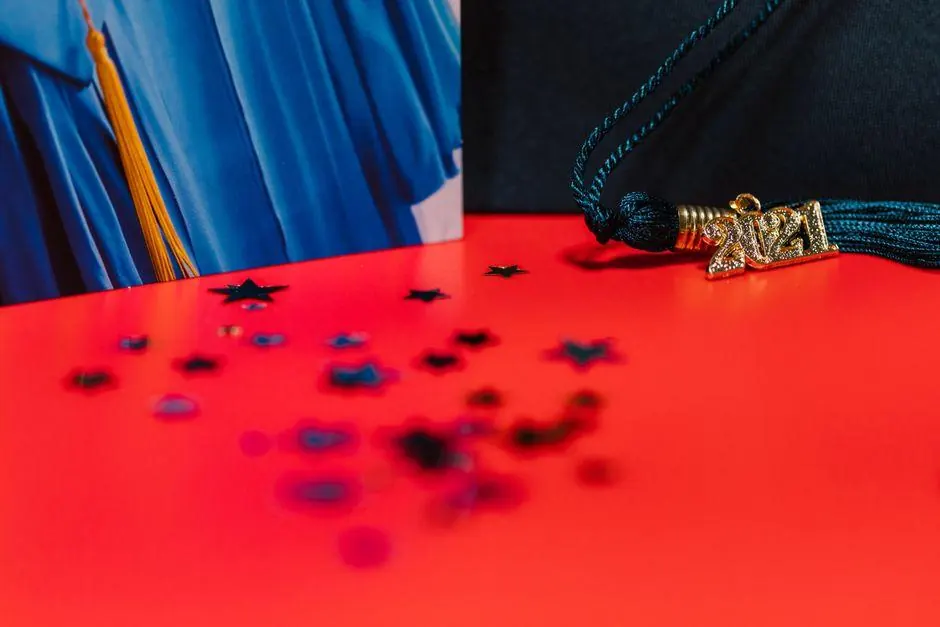 Graduation cap and tassel on a red surface beside a blue gown