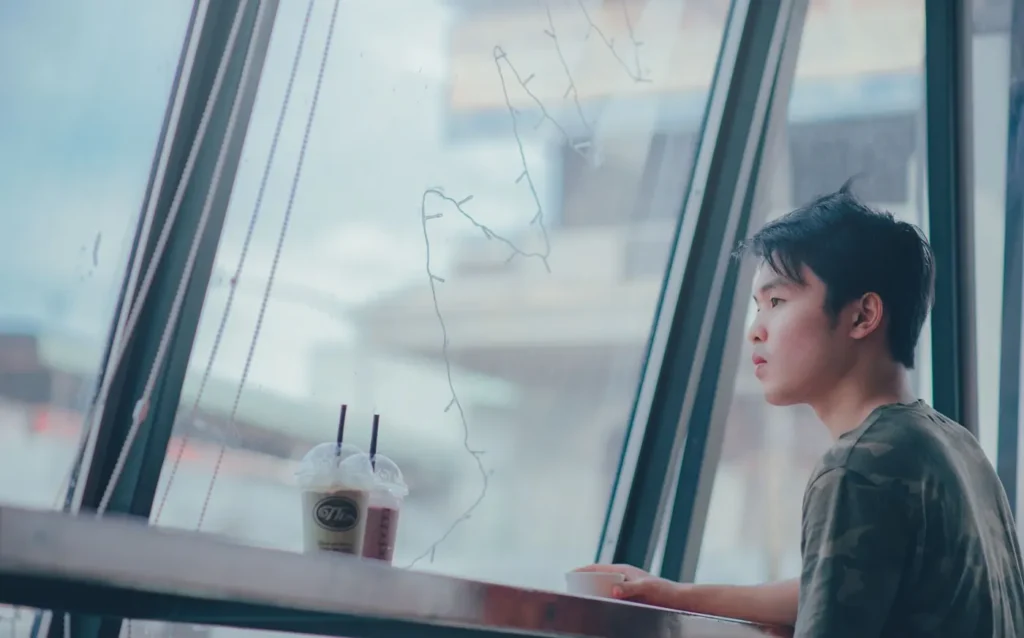 Man seated beside a cafe window with a drink
