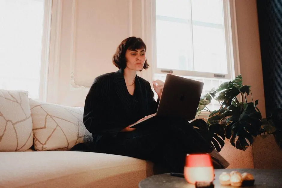 Woman using a laptop on a sofa beside a window