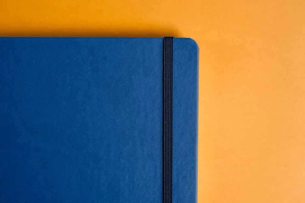 Closed blue notebook secured with a black elastic band on an orange surface