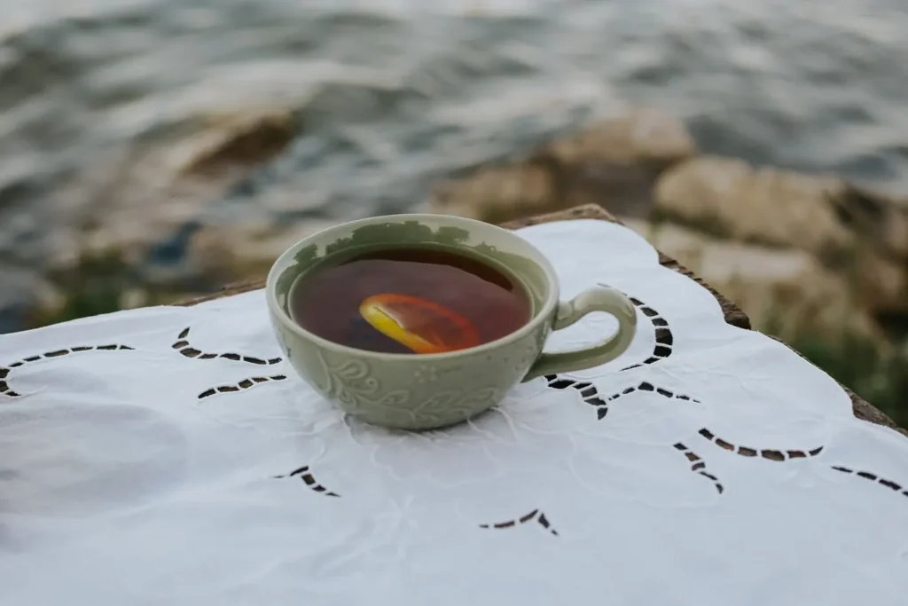 A cup of tea with a lemon slice on white lace cloth beside the water