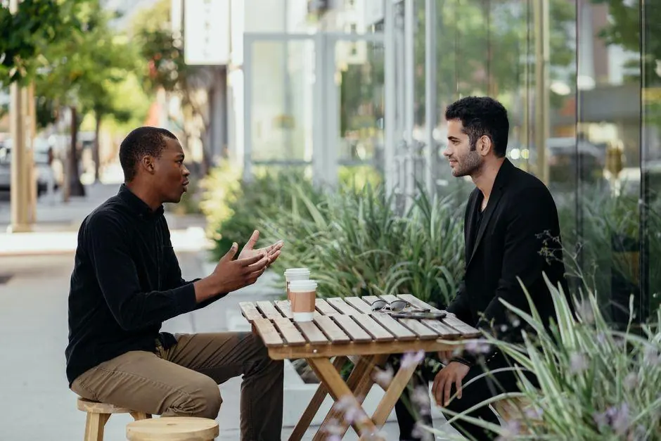 Two men talking at a wooden table outside a cafe