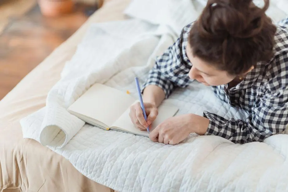 Woman writing in a notebook while lying on a sofa