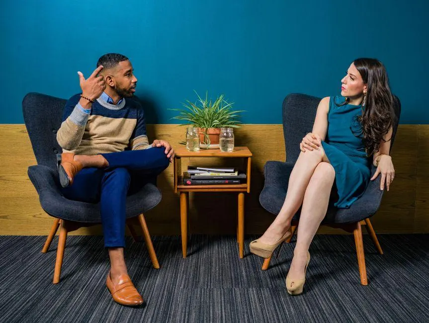 Two adults talking in armchairs beside a small table