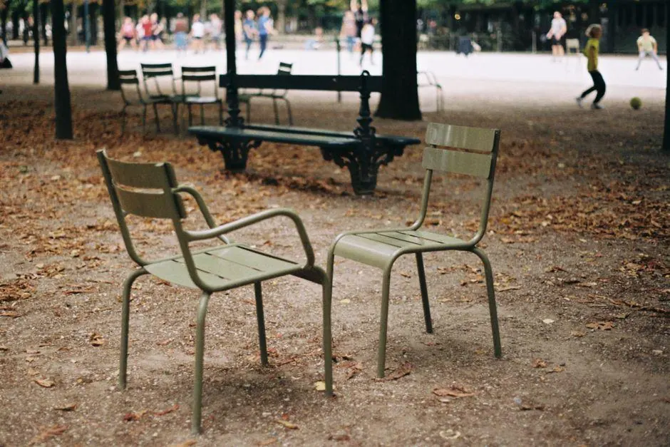 Two empty green chairs facing each other beneath trees in an autumn park