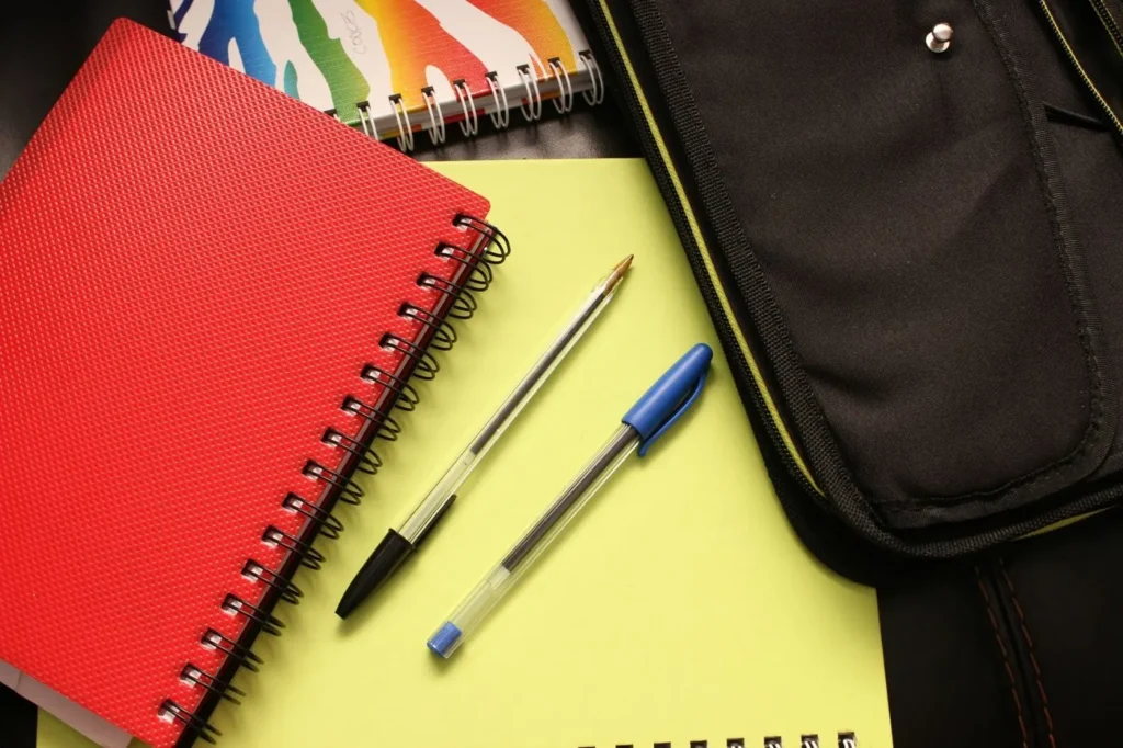 Red and black notebooks with two pens on a yellow surface